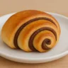 Diabetic-friendly chocolate wassant pastry with golden-brown swirls and rich dark chocolate layers, served on a white ceramic plate over a wooden background